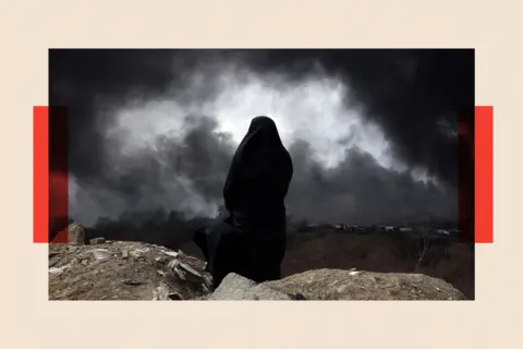EPA/Shutterstock A view from the back of a woman wearing a chador, who surveys the scene as black smoke billows across the landscape