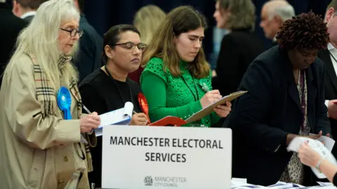 PA Media Three female election observers watch as votes are counted in the Gorton and Denton by-election