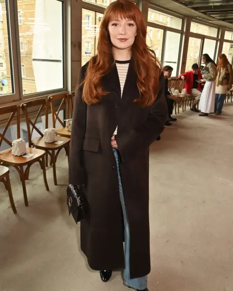 Dave Benett/Getty Images Nicola Roberts stands in front of a row of chairs, wearing a long brown coat