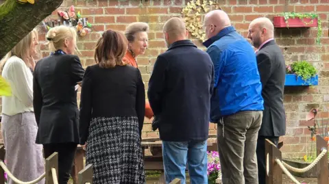 Princess Anne greats three men and three women in a garden area