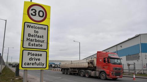 A red lorry drives on the road beside a 30 mph sign that says Welcome to Belfast Harbour Estate
