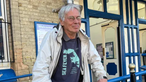 Clare Worden/BBC Commuter Jim Ring is wearing a blue t-shirt and a white waterproof coat. 