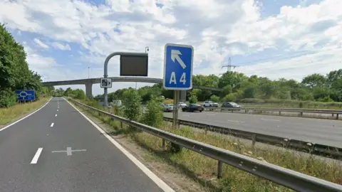 M4 motorway eastbound near Theale with slip road leading off to the A4. It is a bright, sunny day.