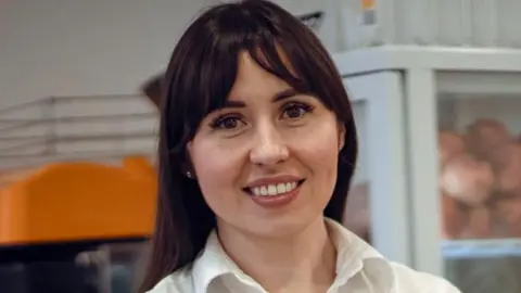 Maryna with brown hair and wearing a white shirt smiles at the camera