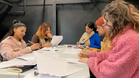 Five people sitting around a white-topped table reading scripts.
(L to R: Aizah Khan, Shazia Bibi, Sameena Hussain, Umar Butt, and Jade Fearnley).