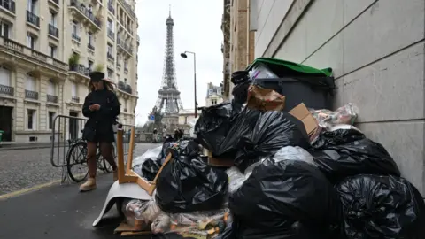 Getty Images Garbage cans overflowing with trash on the streets as collectors go on strike in Paris, France on March 13, 2023. Garbage collectors have joined the massive strikes throughout France against pension reform plans.