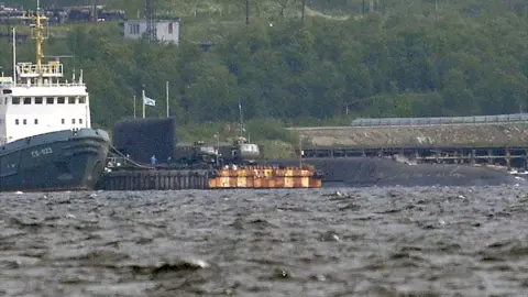 Getty Images A rescue tugboat (L) and the BS-136 Orenburg ballistic missile submarine (R) carrying a nuclear deepwater station of Project 10831 at the Russian Northern Fleet's base