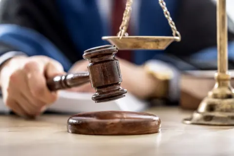 A close up shot of a wooden mallet held over a wood base, in a tribunal setting.