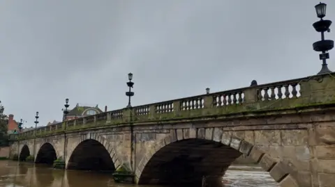 Shropshire Council A bridge featuring four semi-circular arches above the river. At least four street lamps are on the bridge, which goes from left to right on the photo.