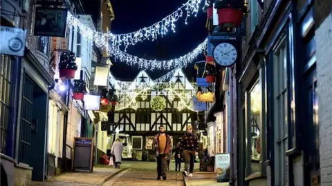 The photos shows a street in Lincoln, shops on either side and Christmas lights lit up. There are some people walking towards the camera. 