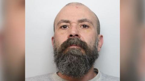 Trevor Evans with a thick beard and grey jumper appearing in police custody