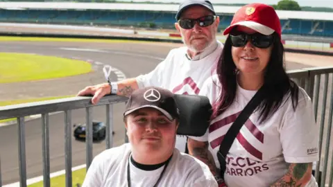 Family Handout Dakota and his mother and grandfather at the side of the racetrack looking towards the camera. All are wearing caps with car manufacturers on them.