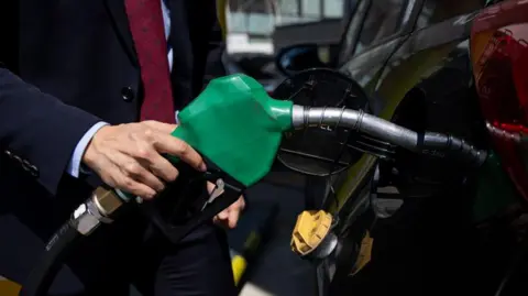 Getty Images A driver dressed in a suit and tie refuels his vehicle using a green petrol pump 