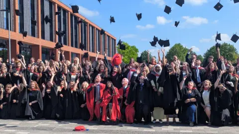 A large group of people in formal wear are pictured throwing their mortar board hats in the air