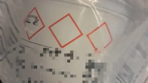 Metropolitan Police A white container is seen with a corrosive substance warning on its side