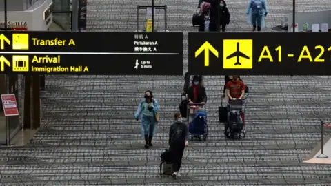 Getty Images Travellers wearing protective mask walk along the transit area of Changi International Airport terminal on December 15, 2020 in Singapore.