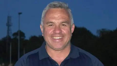 Sgt Matt Ratana smiling with short grey hair wearing a navy blue polo shirt.