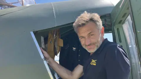 Richard Santos -the owner and pilot of the Gentle Annie - a man in a navy blue t-shirt climbing out of the cockpit of a green plane.