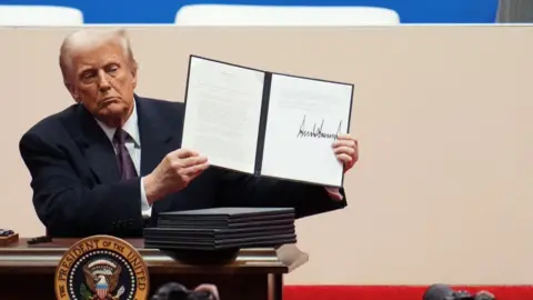 Getty Images Trump shows off an executive order after signing it