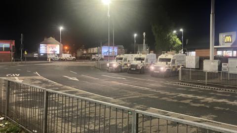 A wide shot of a street at Broadway Roundabout - three police Land Rovers are in the middle distance