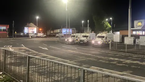 BBC A wide shot of a street at Broadway Roundabout - three police Land Rovers are in the middle distance