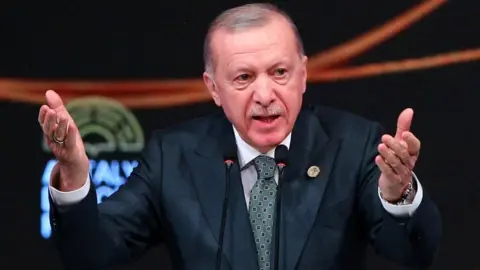 Reuters Turkey's president, dressed in a suit, gestures with his hands out to his audience