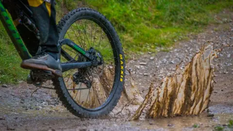 A mountain bike's rear wheel with mud splashing up in the air