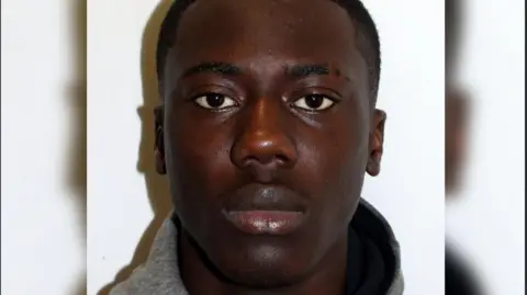 Met Police Tyrese Osei-Kofi police mugshot. He is wearing a grey top and is looking at the camera