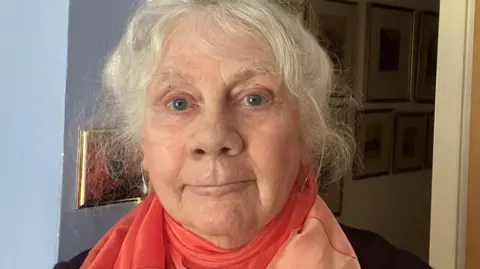 Fiona Cameron A selfie of a woman with white hair. She is wearing an orange scarf. 
