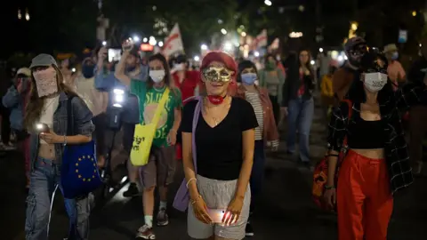 NurPhoto via Getty Images Georgians march in the dark, with a woman wearing a mask and a black T-shirt closest to the picture