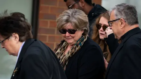 PA Media Julia Amess (centre) the widow of Conservative MP Sir David Amess, accompanied by the Rev Clifford Newman (right) of Belfairs Methodist Church, during a visit to view flowers and tributes left for her late husband at the church in Eastwood Road North, Leigh-on-Sea, Essex, where he died after being stabbed several times during a constituency surgery on Friday.