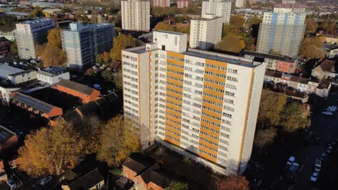 An aerial shot of Barton House showing it with yellow cladding and surrounded by other tower blocks 