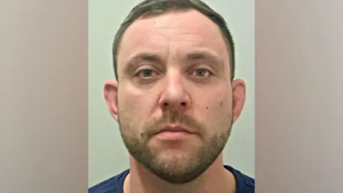 A police mugshot of Grant Eddleston, who has short brown hair and stubble, looking into the camera with a blank expression