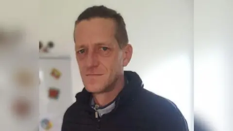 Lincolnshire Police Head and shoulder shot of Vadims Zmicerevskis, who has short hair and is wearing a black zip-up jacket and coat. There is a beige wall in the background and the side of a refrigerator.