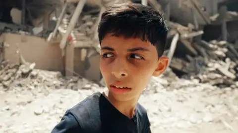 A child in Gaza with rubble behind him