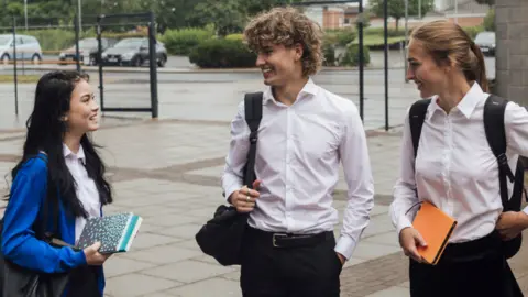 Three teenage students wearing school uniform, standing outside their school at break time.