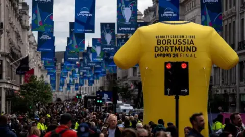 Reuters Crowds walk under flags and behind a giant inflatable yellow football shirt on Regent Street