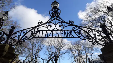 BBC The entrance to Leazes Park which shows a gothic looking gate. There are trees in the background and a blue sky.