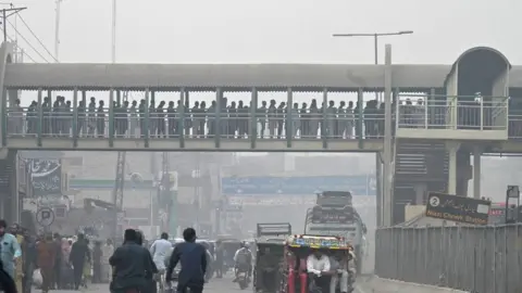 Getty Images Commuters make their way through a busy street amid smoggy conditions in Lahore