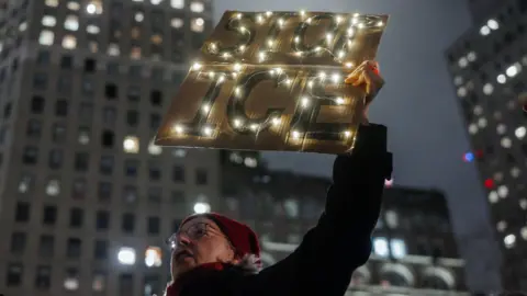 EPA A woman is holding a sign that reads 'stop ice'. There are glowing fairy lights decorated around the banner. 