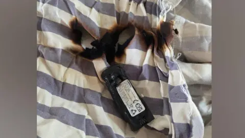 A damaged battery and burnt bedding. The bedding is blue and white stripes.