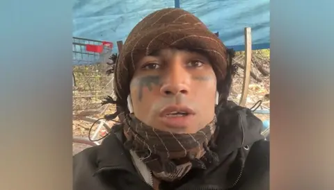 PA Media Fayaz Khan looking at the camera. He is wearing a green bandana and a green coat.