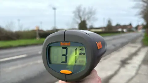 George Carden/BBC A grey radar gun which has a handle and screen which shows the speed of vehicles