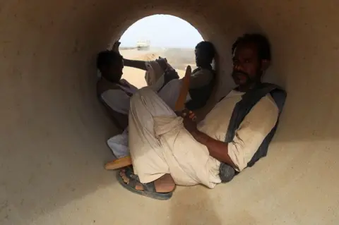 EL TAYEB SIDDIG / REUTERS Three people protect themselves from the sun in a cement pipe.