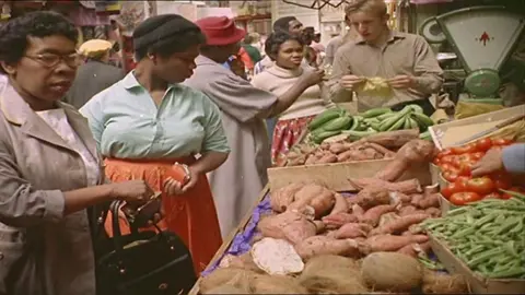 Two women look over a stall selling vegetables in Brixton Market