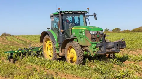 A green tractor parked in a field equipped with a Garford inter-row hoe.