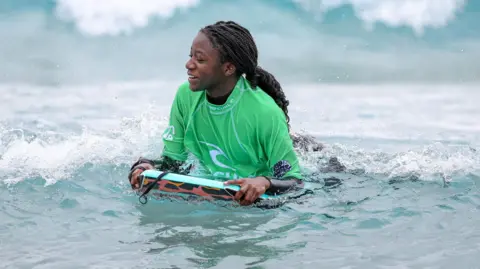 The Wave A teenage girl in a green top bodyboards on a wave at The Wave surfing lake in Bristol