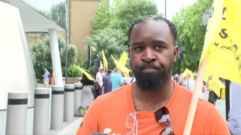 Bearded man in orange shirt with glasses and sunglasses hold a yellow flag