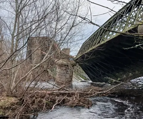 Roddy Robertson A collapsed bridge with a stone pier at an angle and trees in the foreground