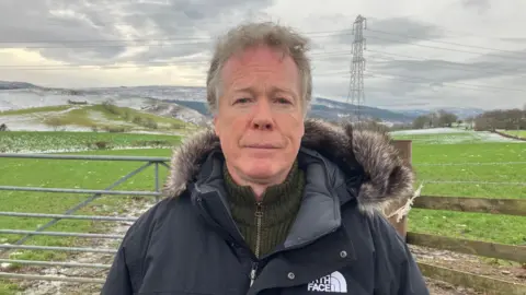 Kevin Sharp looking into the camera with the proposed Battery Energy Storage Systems site behind him. 